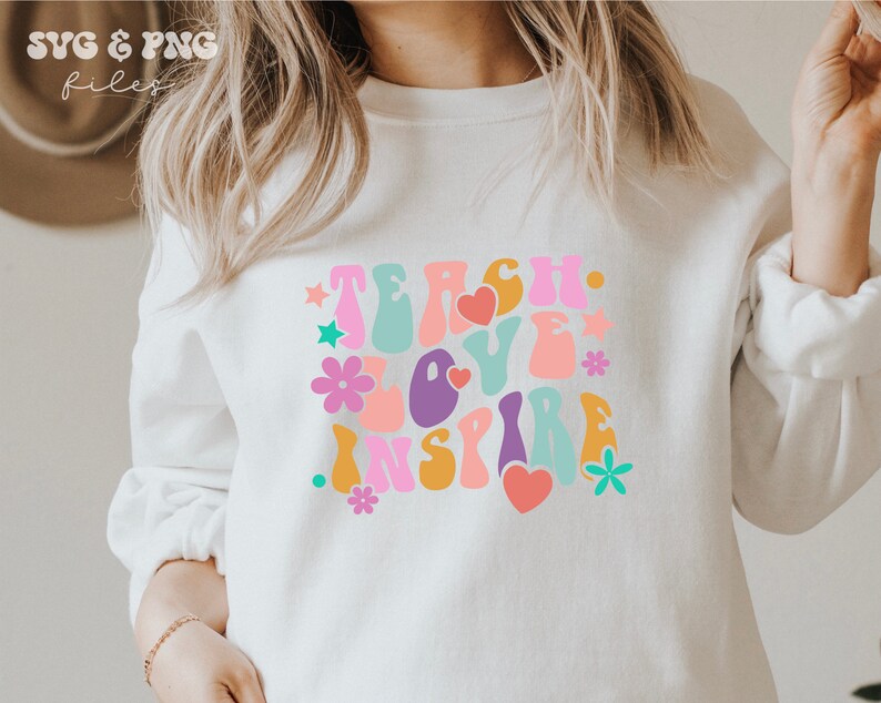 Peut inclure: Sweat-shirt blanc avec un motif graphique color&eacute; qui dit "Teach Love Inspire" dans un style de police r&eacute;tro.