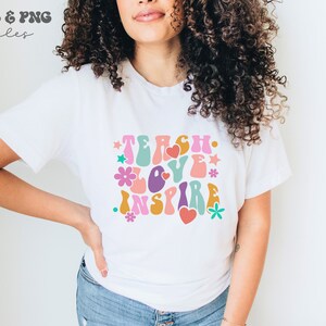 Peut inclure: Un t-shirt blanc avec un graphisme r&eacute;tro qui dit "Teach Love Inspire" en lettres color&eacute;es et ondul&eacute;es avec des fleurs et des c&oelig;urs.