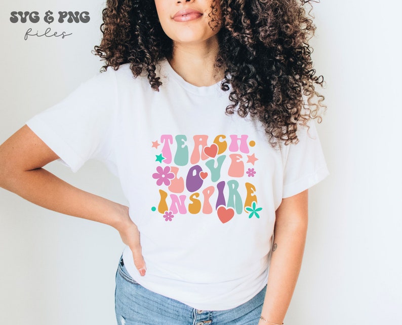 Peut inclure: Un t-shirt blanc avec un graphisme r&eacute;tro qui dit "Teach Love Inspire" en lettres color&eacute;es et ondul&eacute;es avec des fleurs et des c&oelig;urs.