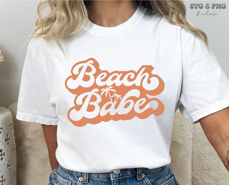 May include: White t-shirt with a peach-colored graphic that says "Beach Babe" in a retro font with palm trees.