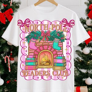 May include: White t-shirt with a festive design. The design features the text "NORTH POLE READERS CLUB" around a pink and gold fireplace with stockings, books, and a bow. A great gift for book lovers during the Christmas season.