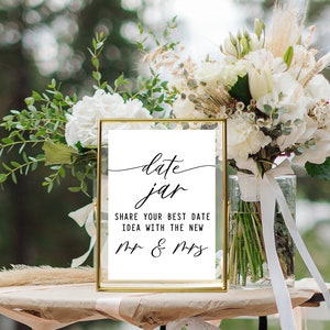 May include: A gold-framed sign with the text "date jar" in cursive script. Below the text, it reads "Share your best date idea with the new Mr. & Mrs."