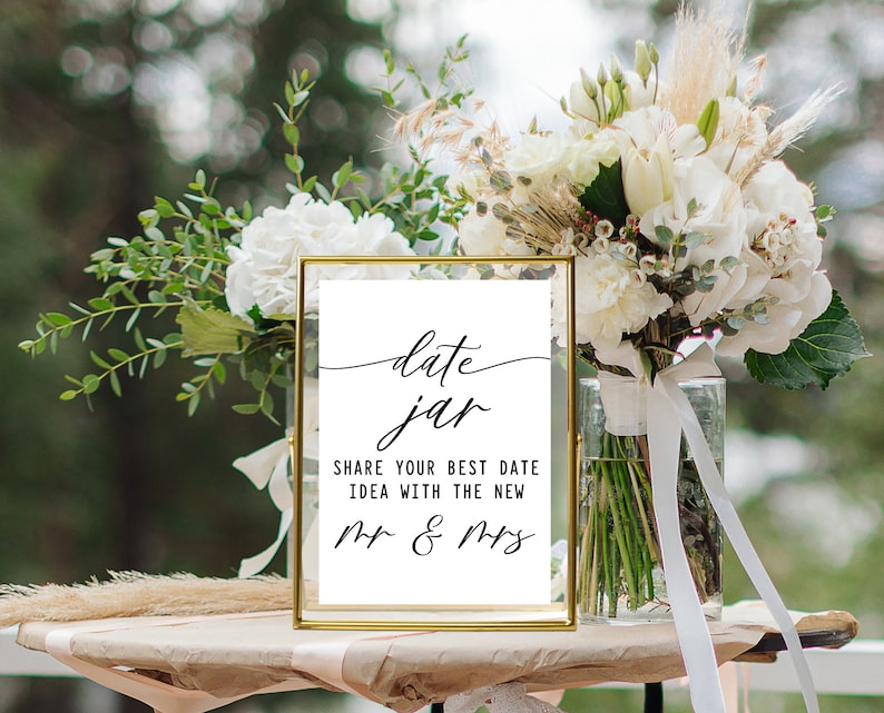 May include: A gold-framed sign with the text "date jar" in cursive script. Below the text, it reads "Share your best date idea with the new Mr. & Mrs."