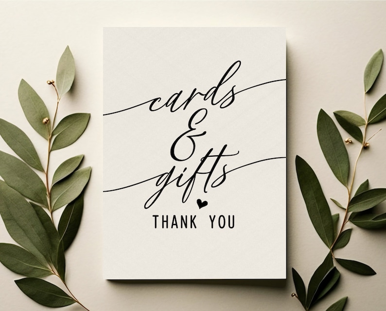 May include: A white card with black calligraphy that reads "cards & gifts thank you". The card is surrounded by green eucalyptus branches.