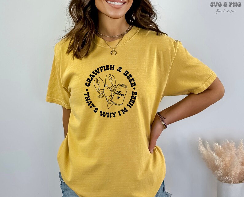 May include: A yellow t-shirt with a black graphic of a crawfish holding a can of beer. The text on the shirt reads "Crawfish & Beer... That's Why I'm Here."