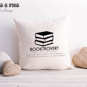 May include: A square off-white throw pillow featuring a black graphic of a stack of three books. Below the books, the text reads BOOKTROVERT (book - tro - vert noun) A person who prefers the company of fictional characters to real people.