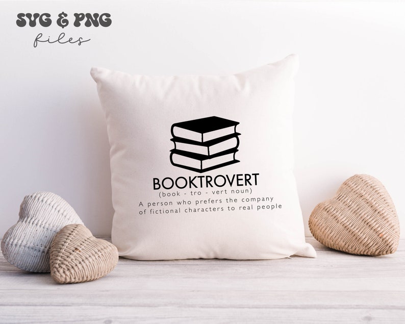 May include: A square off-white throw pillow featuring a black graphic of a stack of three books. Below the books, the text reads BOOKTROVERT (book - tro - vert noun) A person who prefers the company of fictional characters to real people.