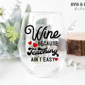 May include: A clear glass wine glass with the text "Wine because teaching ain't easy" in black lettering with red hearts.