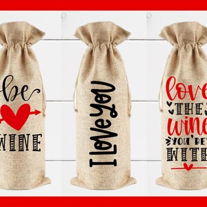 May include: Three burlap wine bottle bags with different Valentine's Day themed sayings. The first bag says "be wine" with a red heart and arrow. The second bag says "I love you". The third bag says "love the wine you're with".
