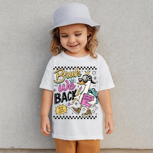 May include: White t-shirt with a graphic of a cartoon duck wearing sunglasses, a backpack, and holding a notebook. The shirt has the words "Bruh We Back" and "Day One Drama". The shirt is worn by a young child.