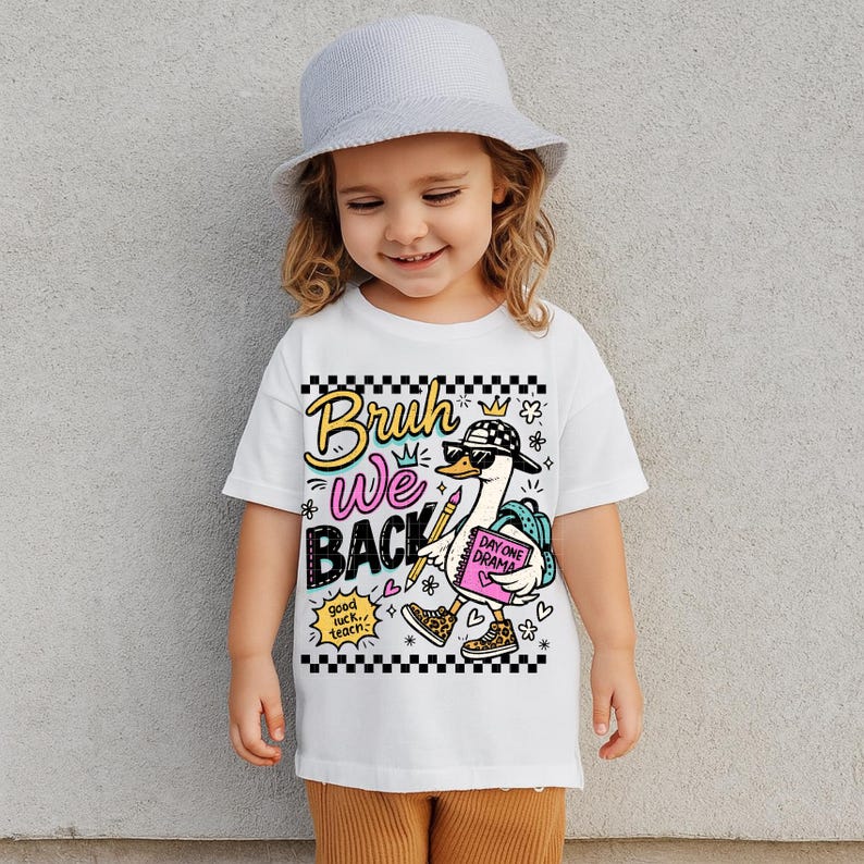 May include: White t-shirt with a graphic of a cartoon duck wearing sunglasses, a backpack, and holding a notebook. The shirt has the words "Bruh We Back" and "Day One Drama". The shirt is worn by a young child.