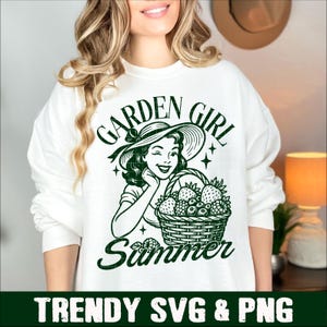 Puede incluir: Sudadera blanca con un dise&ntilde;o verde de una mujer con sombrero de sol, gui&ntilde;ando un ojo y sosteniendo una cesta de bayas. El texto dice "GARDEN GIRL Summer". Debajo del dise&ntilde;o est&aacute; el texto "TRENDY SVG & PNG".