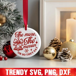 May include: White Christmas ornament with red text that reads "The more, the merrier or so they say". The ornament features a red bow and two bells.