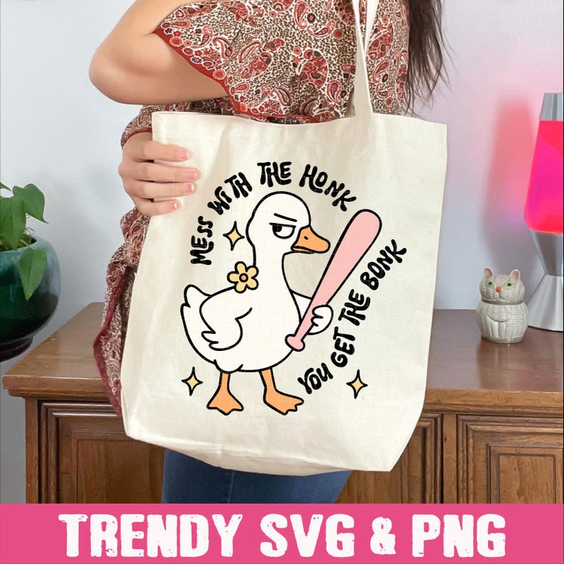 Peut inclure: Sac fourre-tout cr&egrave;me avec un dessin de canard tenant une batte de baseball rose. Le texte dit "MESS WITH THE HONK YOU GET THE BONK". Le bas du sac affiche le texte "TRENDY SVG & PNG".