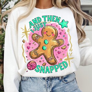 May include: White sweatshirt featuring a gingerbread man design and the text "AND THEN I JUST SNAPPED" in green. The gingerbread man is gold-outlined and set against a pink backdrop with hearts and stars.