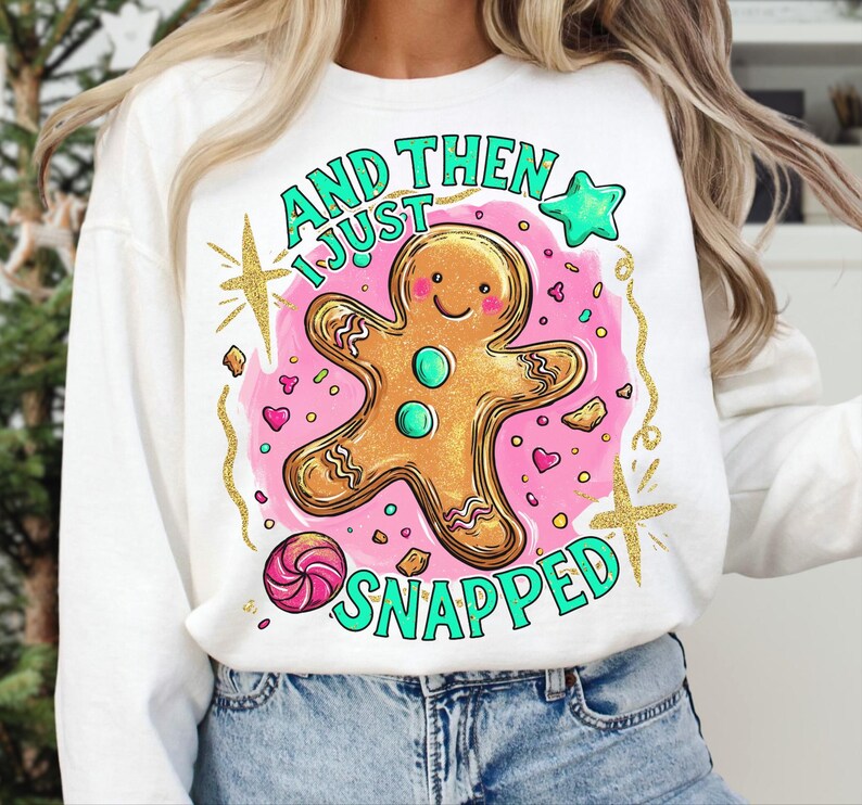 May include: White sweatshirt featuring a gingerbread man design and the text "AND THEN I JUST SNAPPED" in green. The gingerbread man is gold-outlined and set against a pink backdrop with hearts and stars.