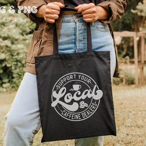May include: A black tote bag with a white circle design that says "Support Your Local Caffeine Dealers" with a coffee cup graphic inside the circle.