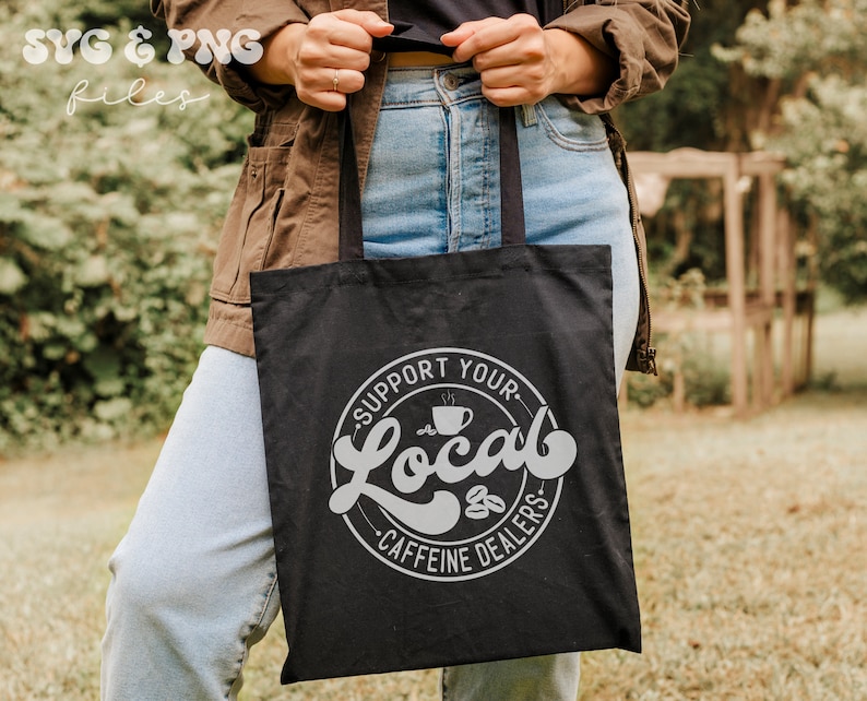 May include: A black tote bag with a white circle design that says "Support Your Local Caffeine Dealers" with a coffee cup graphic inside the circle.