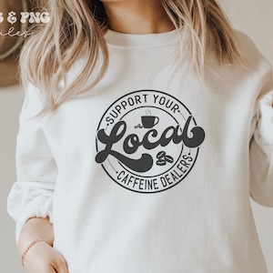 May include: White sweatshirt with a black circle graphic that says "Support Your Local Caffeine Dealers" with a coffee cup and coffee beans inside the circle.