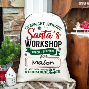 May include: A cream-coloured drawstring canvas sack featuring red, green, and black text that reads: OVERNIGHT SERVICE Santa's WORKSHOP SPECIAL DELIVERY for Mason DO NOT OPEN BEFORE DECEMBER 25TH, accented with small black snowflake and star icons.