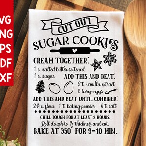 May include: A white tea towel with black text that reads "Cut Out Sugar Cookies". The text includes a recipe for sugar cookies with instructions to cream together butter and sugar, add vanilla extract and eggs, and then add flour, baking powder, and salt. The recipe also includes instructions to chill the dough for at least 2 hours, roll the dough to 1/4 inch thickness, and bake at 350 degrees Fahrenheit for 9-10 minutes.