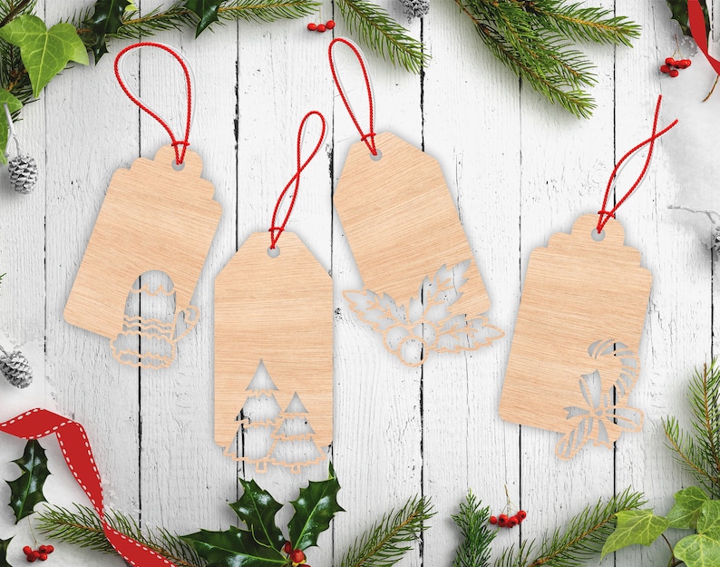 May include: Four light-coloured wooden gift tags with red string loops. Each tag features a unique laser-cut design at the bottom: a mitten, two pine trees, a holly sprig with berries, and a candy cane with a bow, all with a smooth wood grain finish.