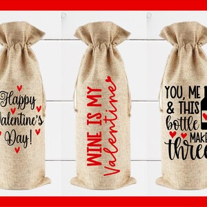 May include: Three burlap wine bottle gift bags with different Valentine's Day themed sayings. The first bag says "Happy Valentine's Day!" with red hearts. The second bag says "Wine is my Valentine". The third bag says "You, me & this bottle makes three".