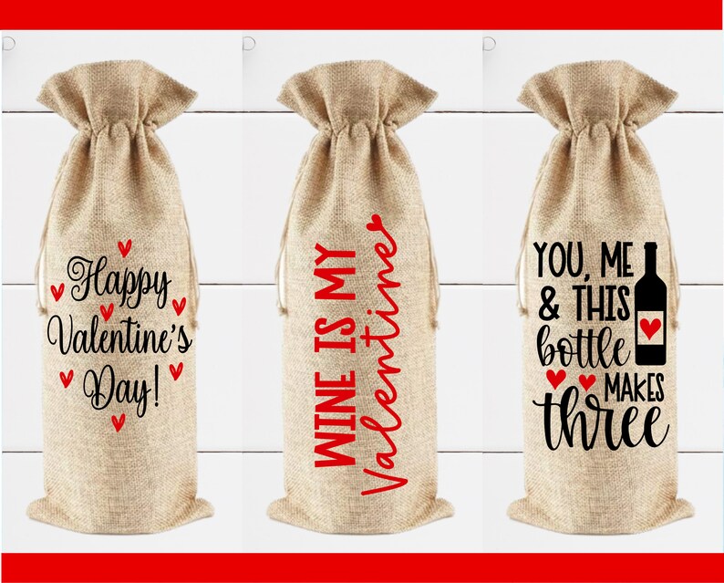 May include: Three burlap wine bottle gift bags with different Valentine's Day themed sayings. The first bag says "Happy Valentine's Day!" with red hearts. The second bag says "Wine is my Valentine". The third bag says "You, me & this bottle makes three".