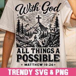 Op de afbeelding: Crèmekleurig T-shirt met een zwarte afbeelding van een kruis op een berg, herten en bomen. De tekst luidt "With God, All Things Are Possible, Matthew 19:26+". De onderste banner zegt "TRENDY SVG & PNG".