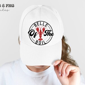 May include: White baseball cap with a black and red design that says "Belle of the Boil" with a lobster illustration.
