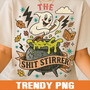 May include: Beige t-shirt with a Halloween-themed graphic. The design features a cartoon ghost stirring a cauldron with the text "THE SHIT STIRRER" on a banner. Additional elements include lightning bolts, stars, and autumn leaves.