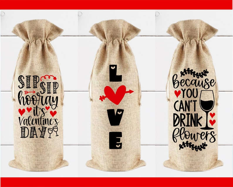 May include: Three burlap wine bottle bags with different Valentine's Day themed designs. The first bag says "Sip Sip Hooray It's Valentine's Day". The second bag says "Love" with a red heart and arrow. The third bag says "Because You Can't Drink Flowers" with a wine glass and hearts.