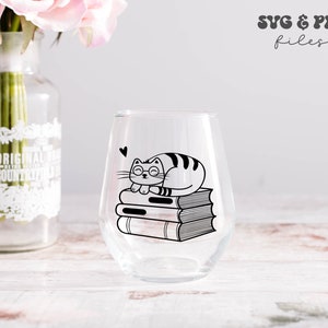 May include: A clear stemless wine glass featuring a black graphic of a cat wearing glasses resting on a stack of three books with a small heart icon above. The text SVG & PNG files is visible in the upper right corner of the image.
