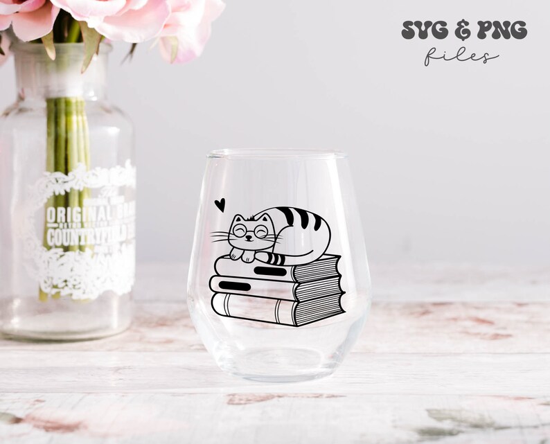 May include: A clear stemless wine glass featuring a black graphic of a cat wearing glasses resting on a stack of three books with a small heart icon above. The text SVG & PNG files is visible in the upper right corner of the image.