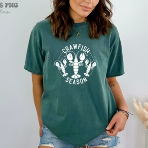 May include: A teal blue t-shirt with a white graphic of crawfish and the text "Crawfish Season".