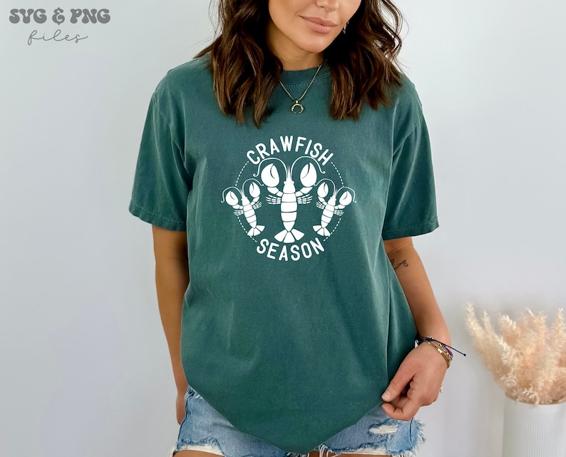 May include: A teal blue t-shirt with a white graphic of crawfish and the text "Crawfish Season".