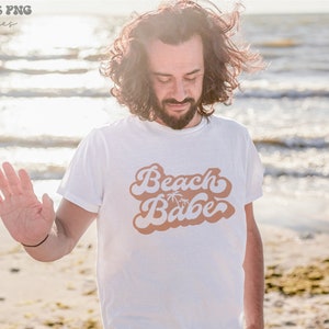 May include: A white t-shirt with a brown retro-style graphic that says "Beach Babe" with palm trees.