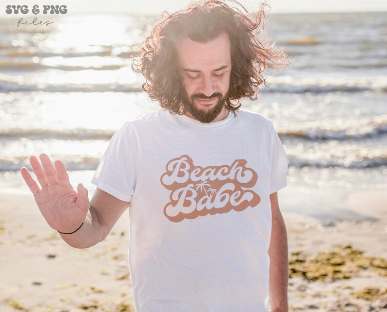 May include: A white t-shirt with a brown retro-style graphic that says "Beach Babe" with palm trees.