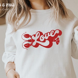 May include: White sweatshirt with a red graphic design of the word "Love" in a retro font with a lobster on either side of the word.