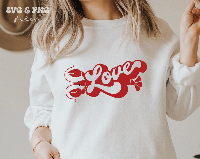 May include: White sweatshirt with a red graphic design of the word "Love" in a retro font with a lobster on either side of the word.