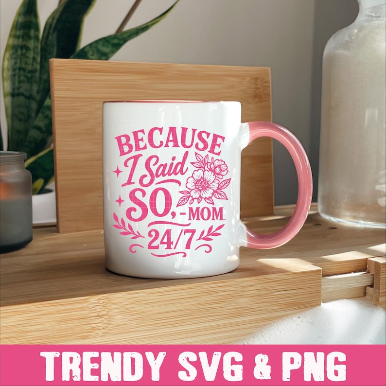 May include: White ceramic mug with a pink design that says "Because I Said So - Mom 24/7". The mug has a pink handle and is sitting on a wooden surface.