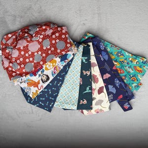Può includere: Assortimento di 10 quadrati di tessuto con vari motivi di ispirazione giapponese. I tessuti presentano una varietà di colori, tra cui rosso, blu, verde e bianco. I motivi includono fiori, forme geometriche e animali.