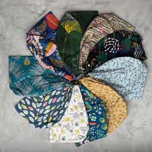 Peut inclure: Une collection de 10 chouchous en tissu colorés avec différents motifs floraux et géométriques. Les chouchous sont disposés en cercle sur une surface grise.