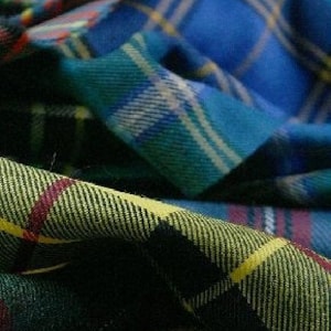 May include: Close-up of folded plaid fabric in various colours. The fabric features a mix of blue, green, yellow, and red intersecting lines. The fabric has a textured appearance, with visible woven threads.