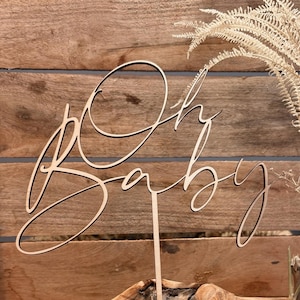 Könnte beinhalten: Holz-Kuchentopper mit den Worten "Oh Baby" in Kursivschrift.