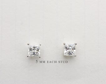 Könnte beinhalten: Zwei quadratische Ohrstecker mit klaren Edelsteinen, jeweils 5 mm groß, werden vor einem weißen Hintergrund gezeigt. Die Ohrringe sind in einem silberfarbenen Metall gefasst, das ihre brillanten Facetten hervorhebt. Der Text "5 mm EACH STUD" ist darunter gedruckt.