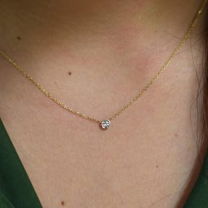 Puede incluir: Un delicado collar de cadena de oro con un pequeño colgante redondo de piedra preciosa transparente.