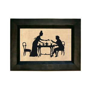 Puede incluir: Una silueta negra de una pareja sentada a una mesa con una tetera y tazas. La imagen est&aacute; enmarcada en un marco negro.