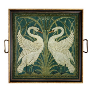 May include: A square serving tray featuring a decorative illustration of two white swans facing each other amidst green reeds and cattails. The tray has a black and gold frame with two metal handles attached to the sides for easy carrying.