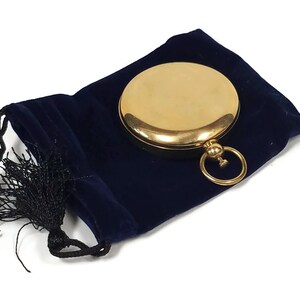 May include: A gold compass with a blue velvet pouch and a black tassel.